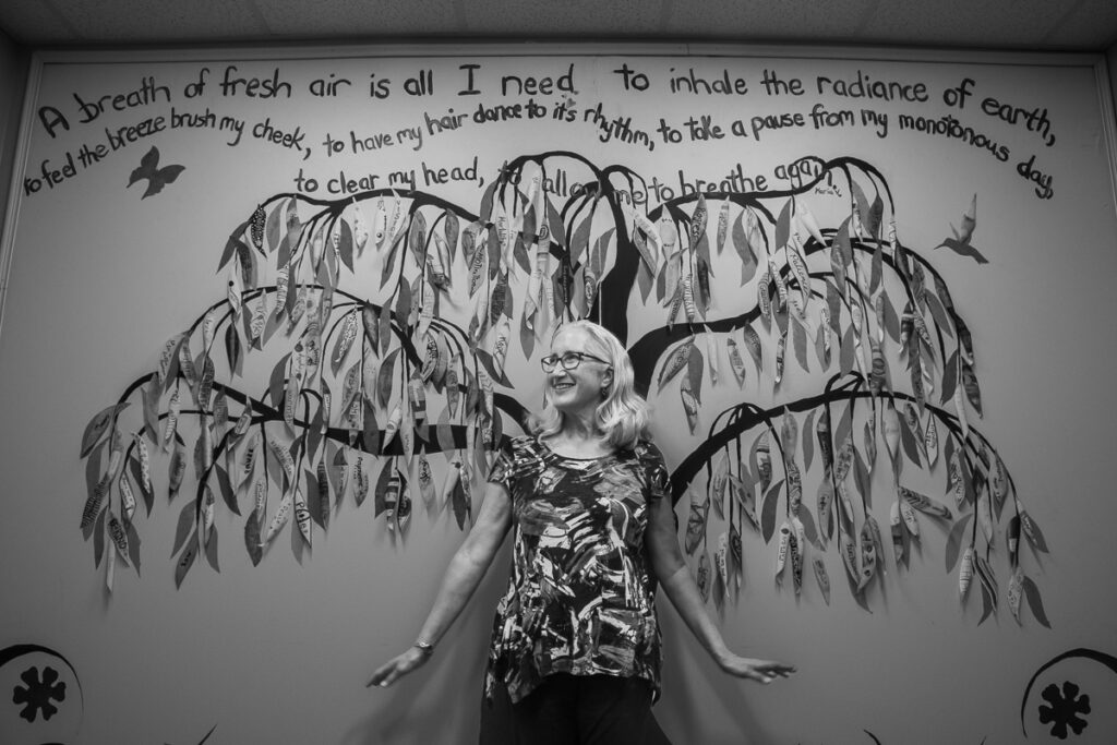 Judy Raybon of Collier High School in Morganville, NJ. Photograph is taken in front of a mural located in the school which includes sentiments made by students in her program. https://www.collierhighschool.com/
